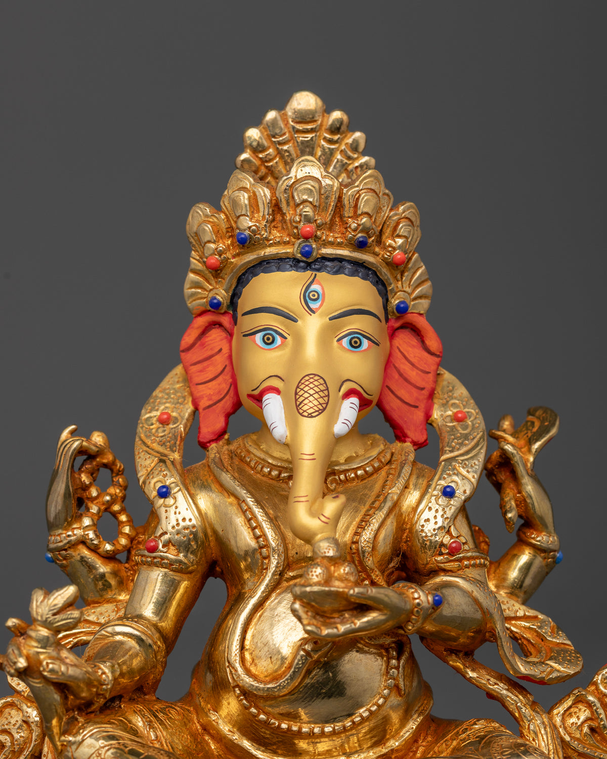 Gold-painted Lord Ganesha face with intricate jewelry and finely detailed gold-gilded ornaments