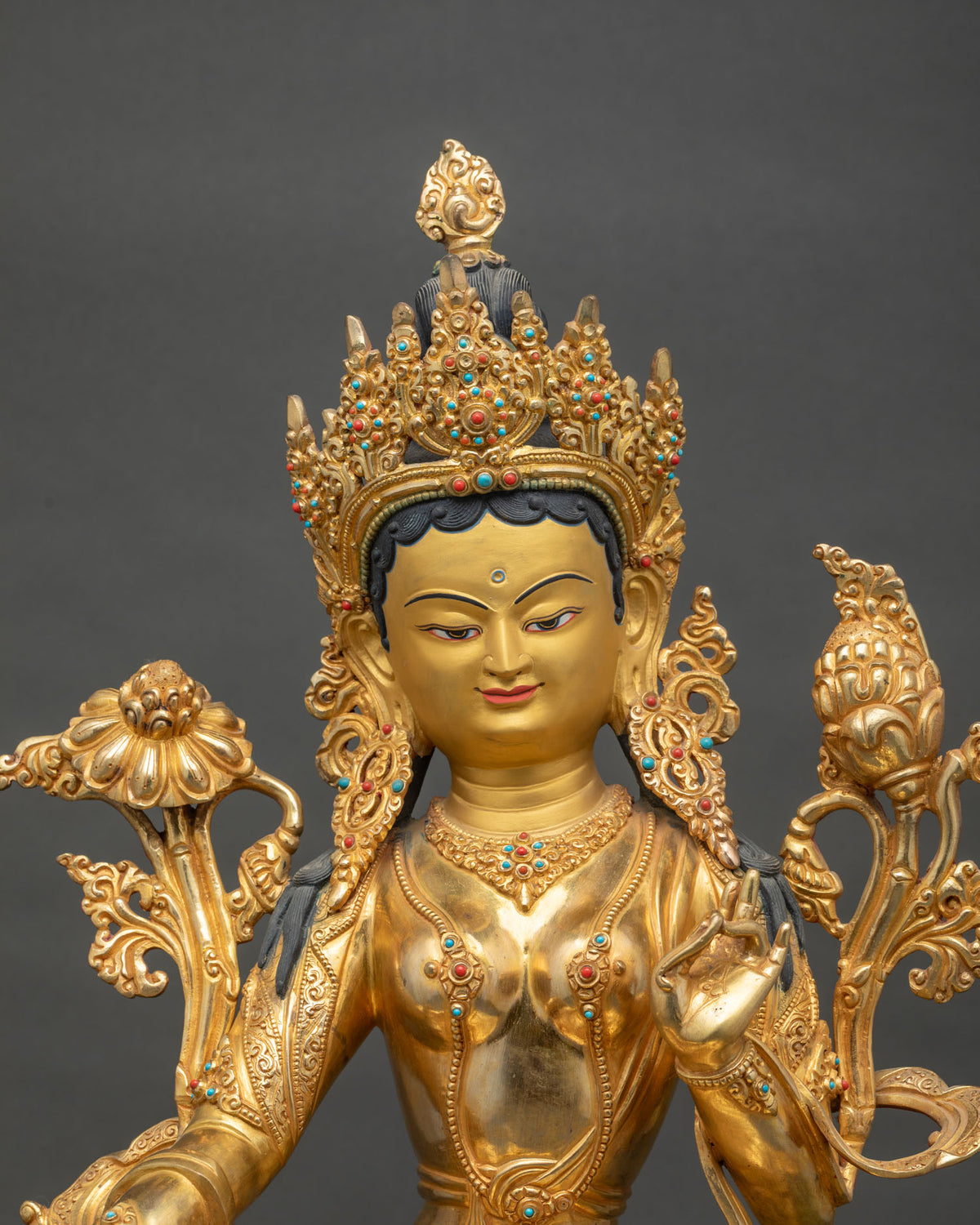 Green Tara statue close up with jeweled crown, gold face and lotus flowers at shoulders