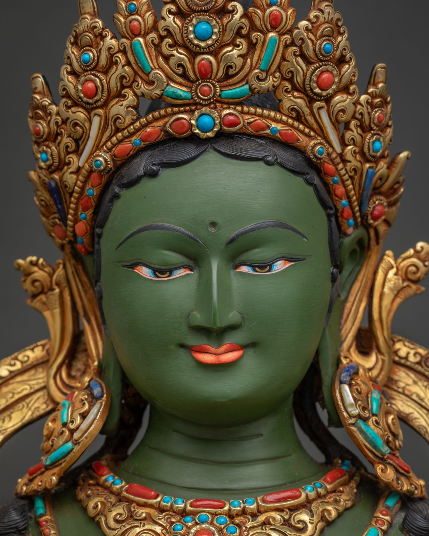 Green Tara statue green face close-up with gold crown and calm expression