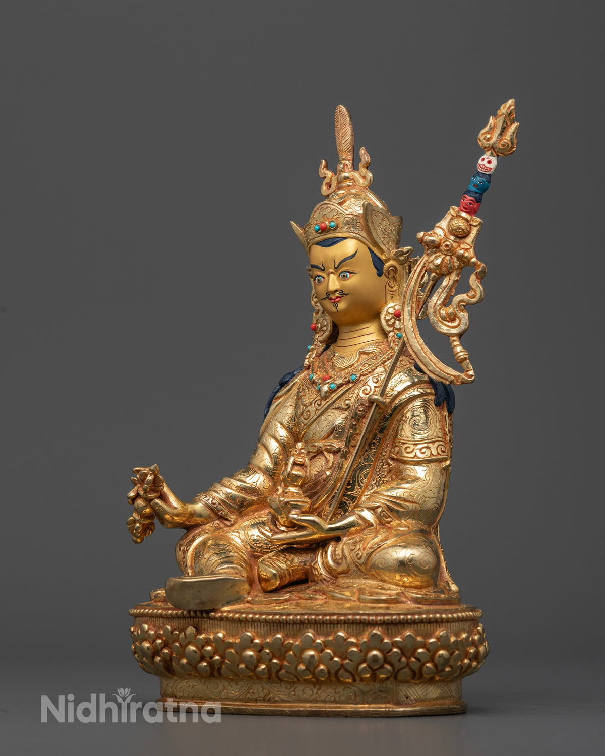 Guru Rinpoche sculpture holding a vajra and kapala with a sacred trident on his shoulder