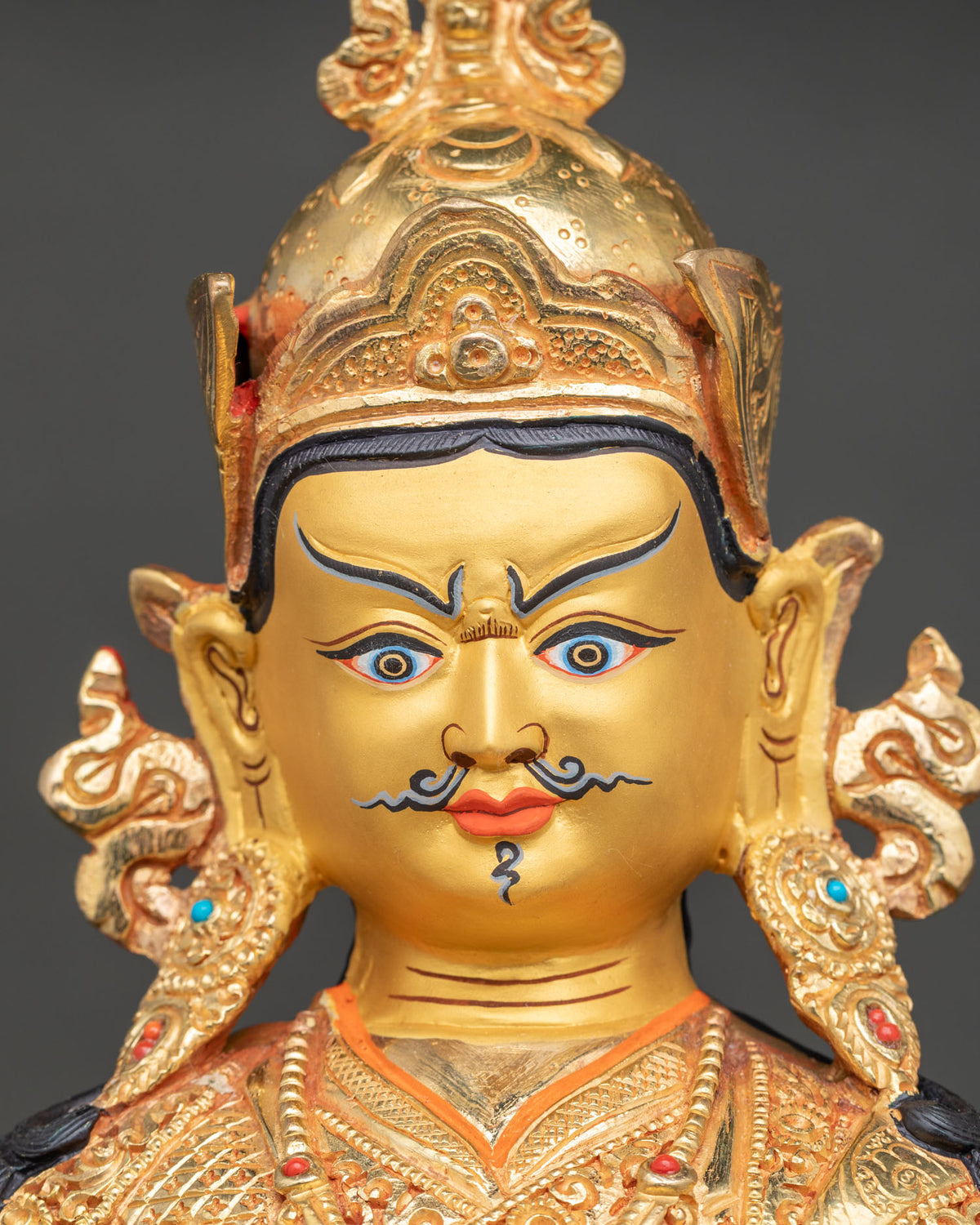 Guru Rinpoche statue close-up featuring a gold-painted face, jeweled lotus hat, and ornate necklace