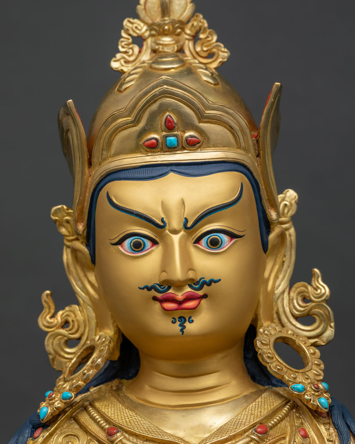Guru Rinpoche statue face close up, gold-painted semi-wrathful expression, turquoise and coral crown