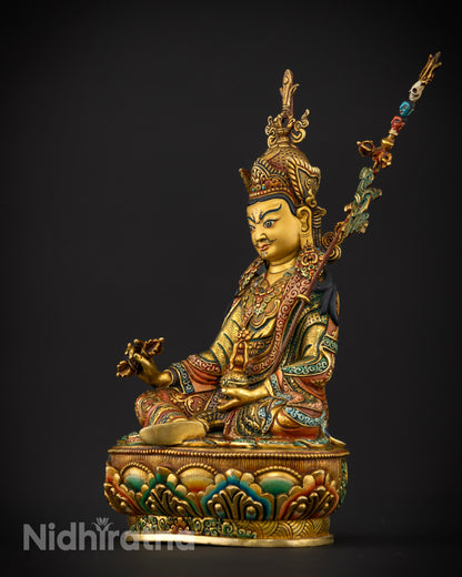 Guru Rinpoche statue with a khatvanga trident staff decorated with symbolic skulls and a flowing banner.