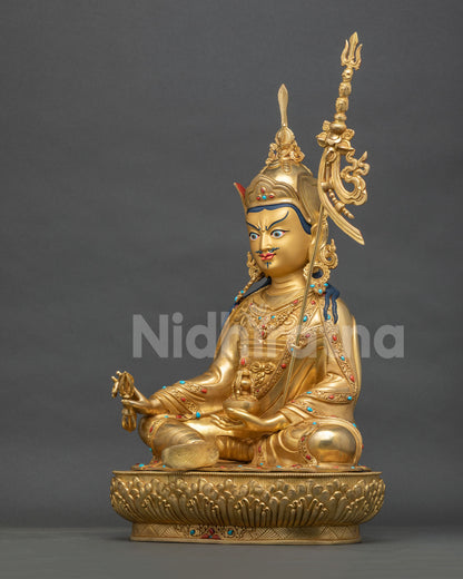 Guru Rinpoche statue left side view, jeweled robes and khatvanga staff, gold fire-gilded copper