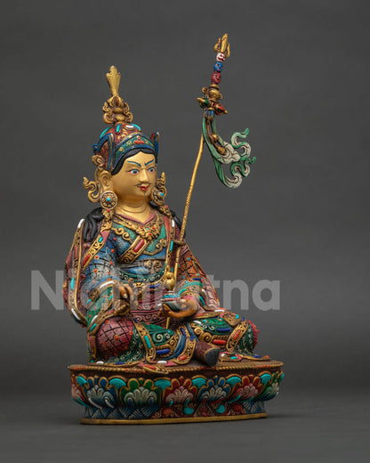 Guru rinpoche statue seated in royal ease on lotus throne holding vajra and skull cup.