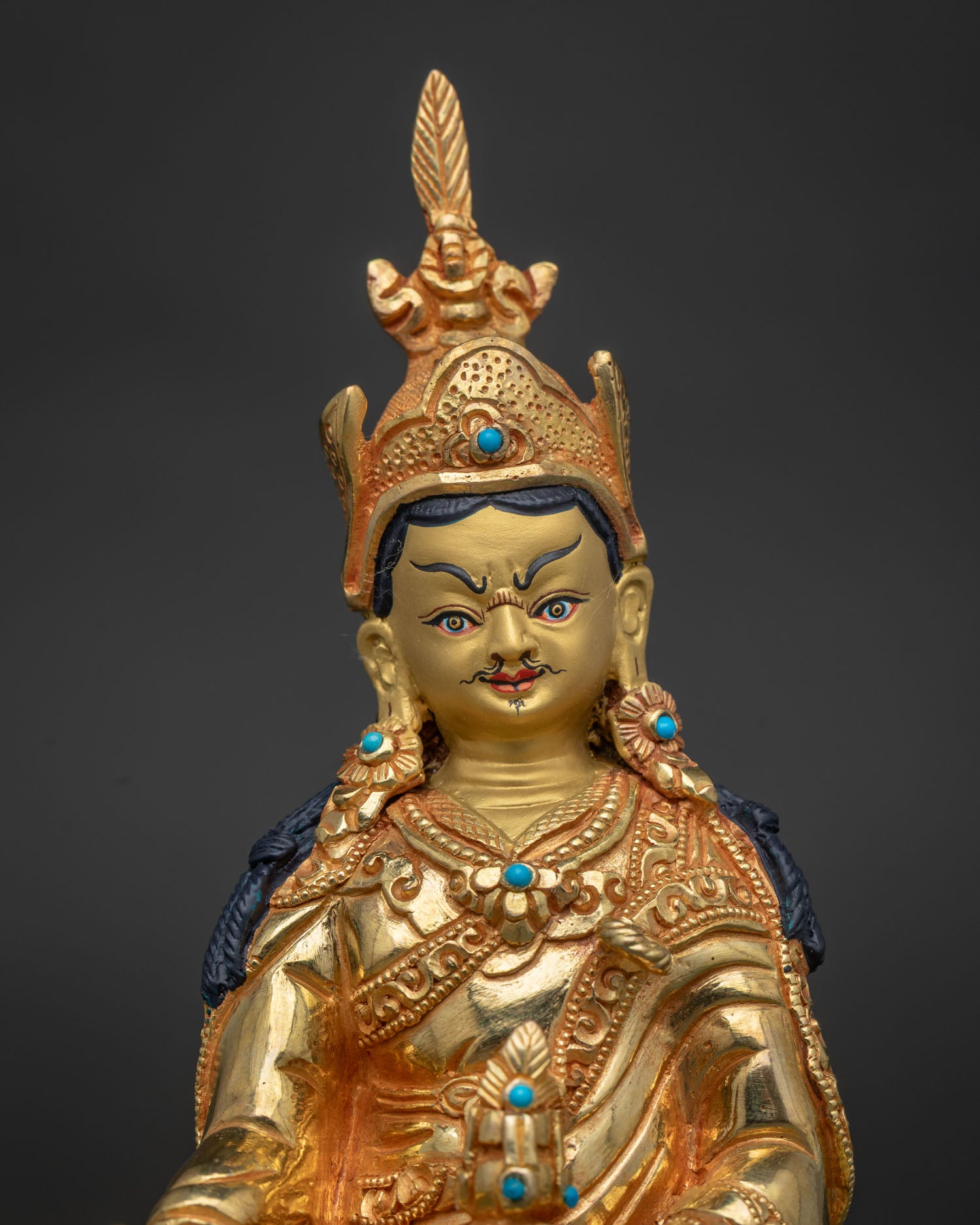 Guru Rinpoche statue showing gold painted face and semi precious stone details.