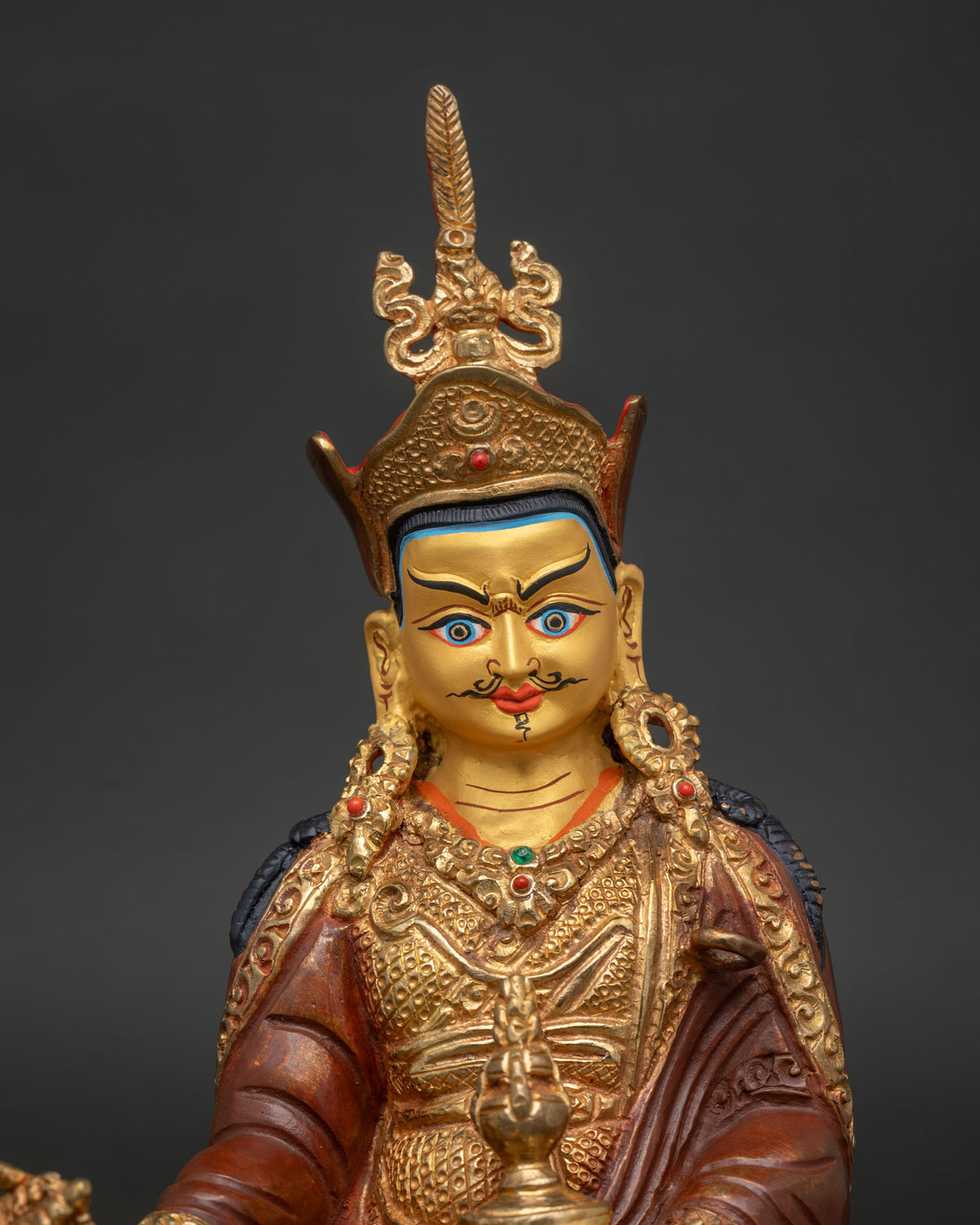 Guru Rinpoche statue with 24K gold painted face seated in royal ease on an ornate lotus throne.
