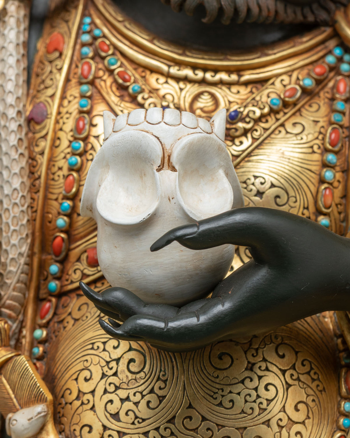Kapala skull cup in the hand of Mahakala Bernagchen with gold hand-chased chest and turquoise beads