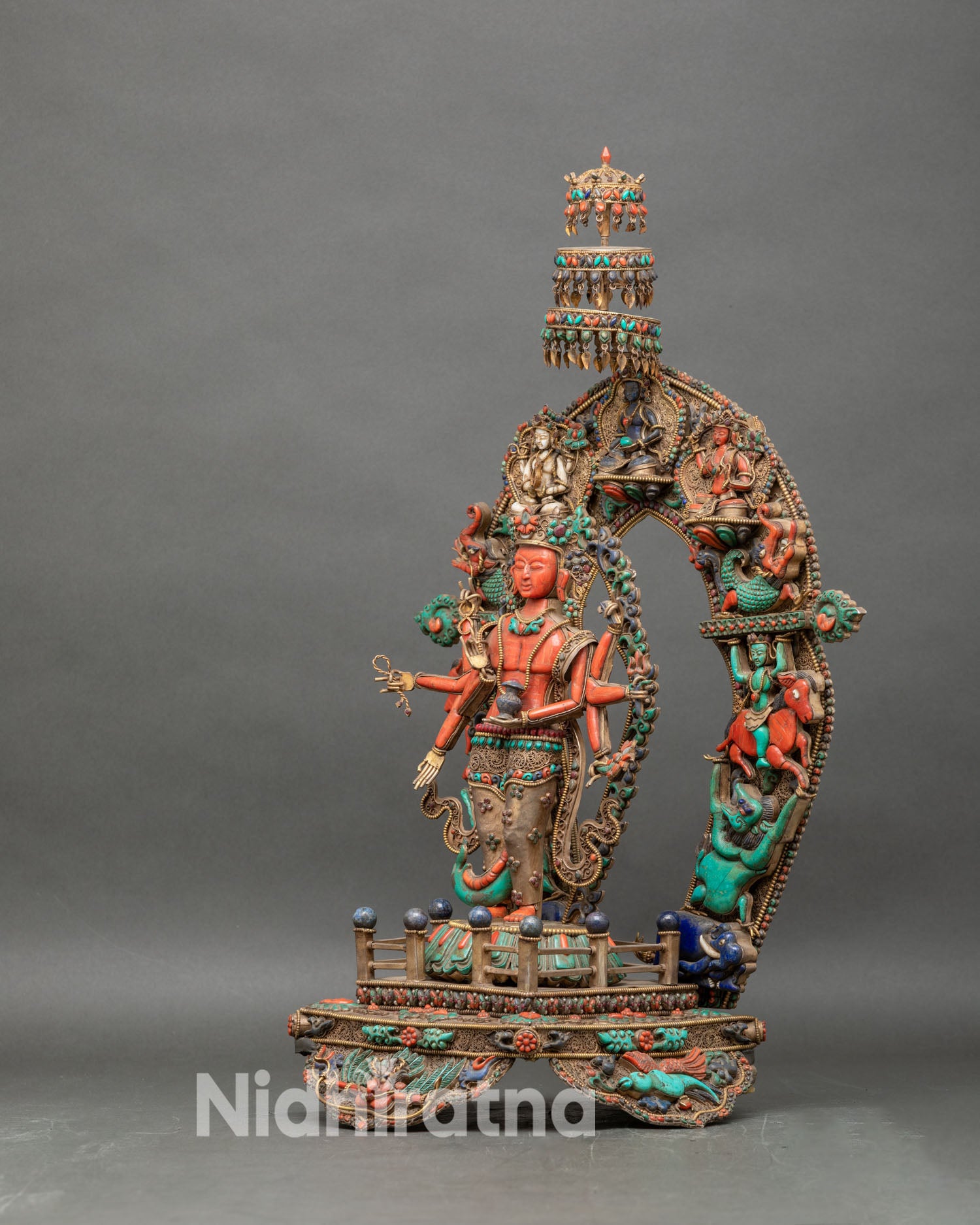 Left profile of coral Chenrezig statue displaying gemstone inlay and ornate gold parasol