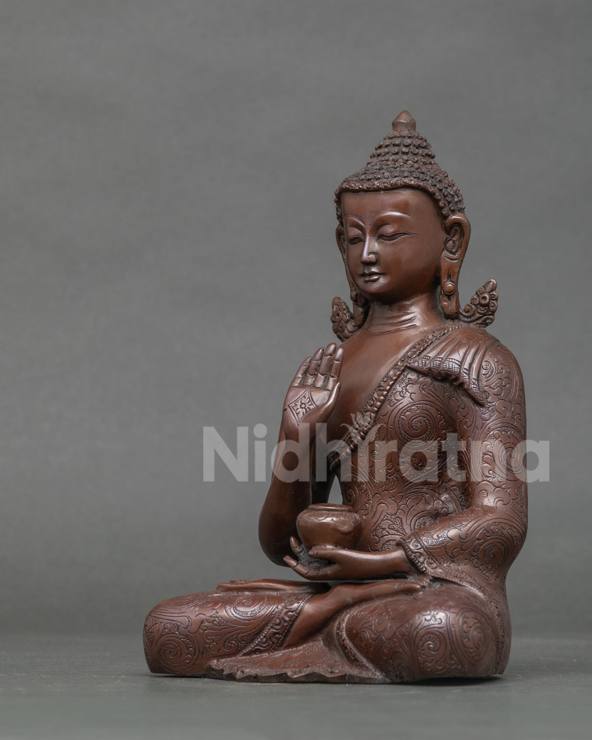 Left side view of oxidized copper Amoghasiddhi Buddha statue with carved floral robe