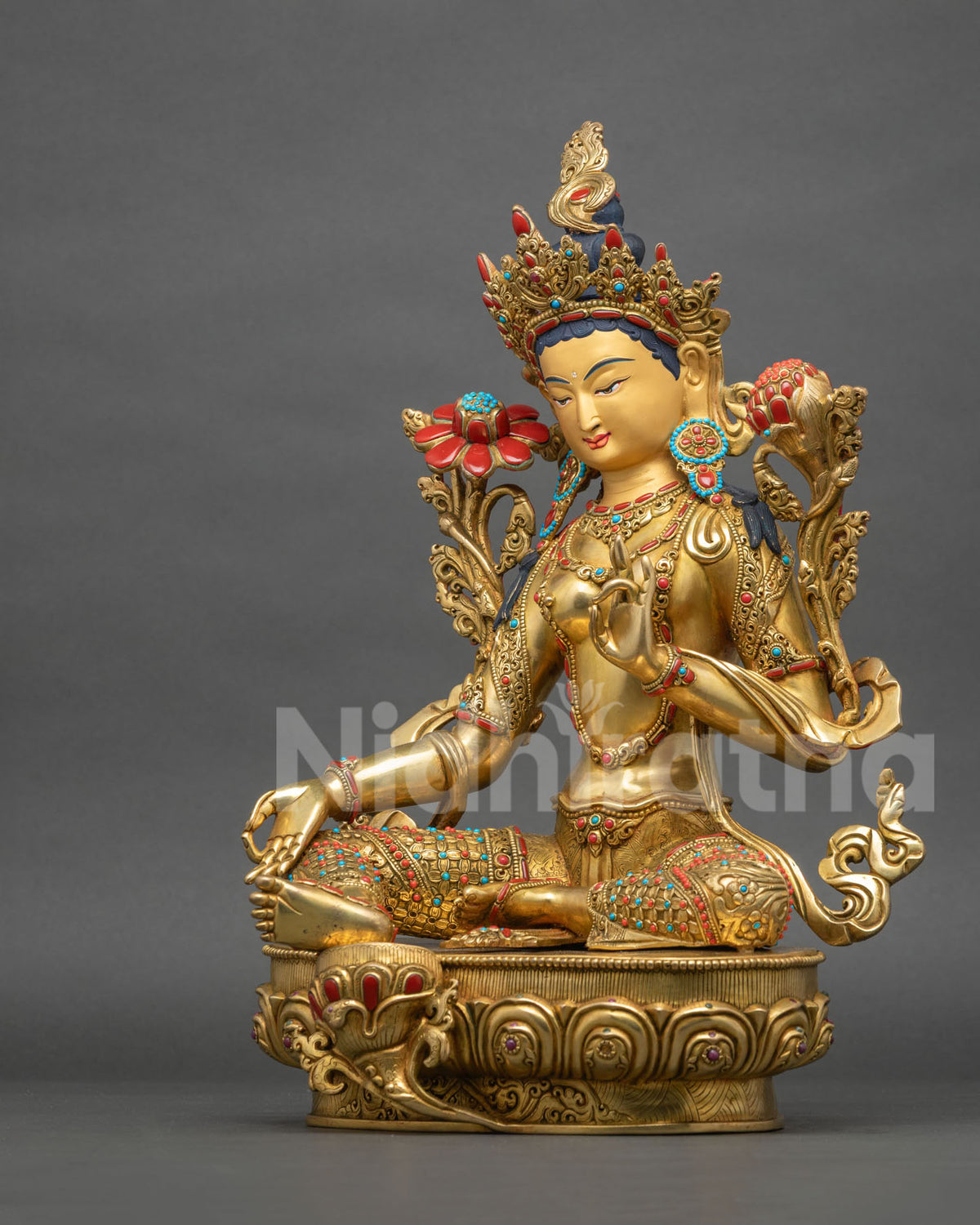 Left side view of seated Green Tara statue with varada mudra and blooming lotus stems on gold throne