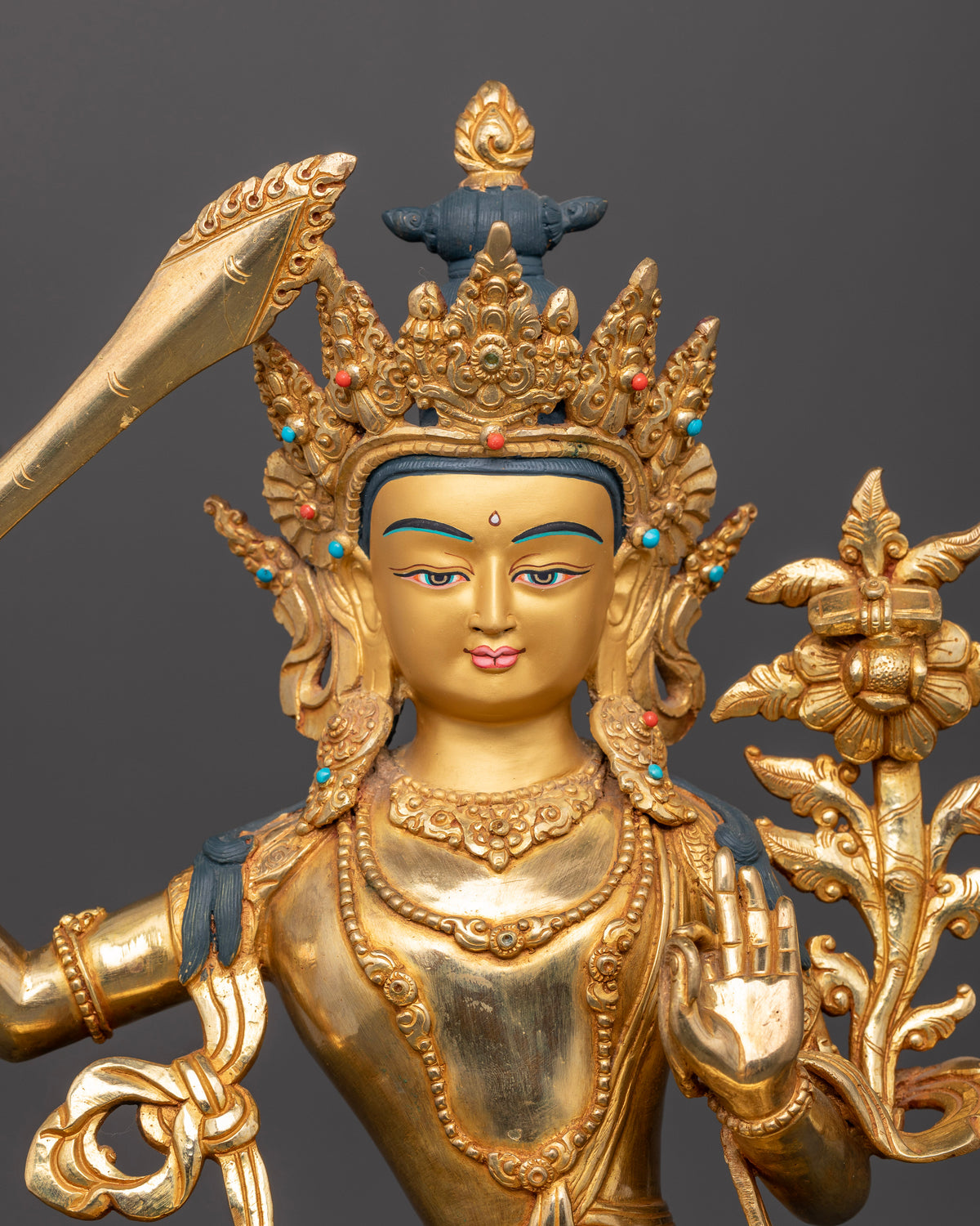 Manjushri statue 24K gold painted face semi precious stones close up.