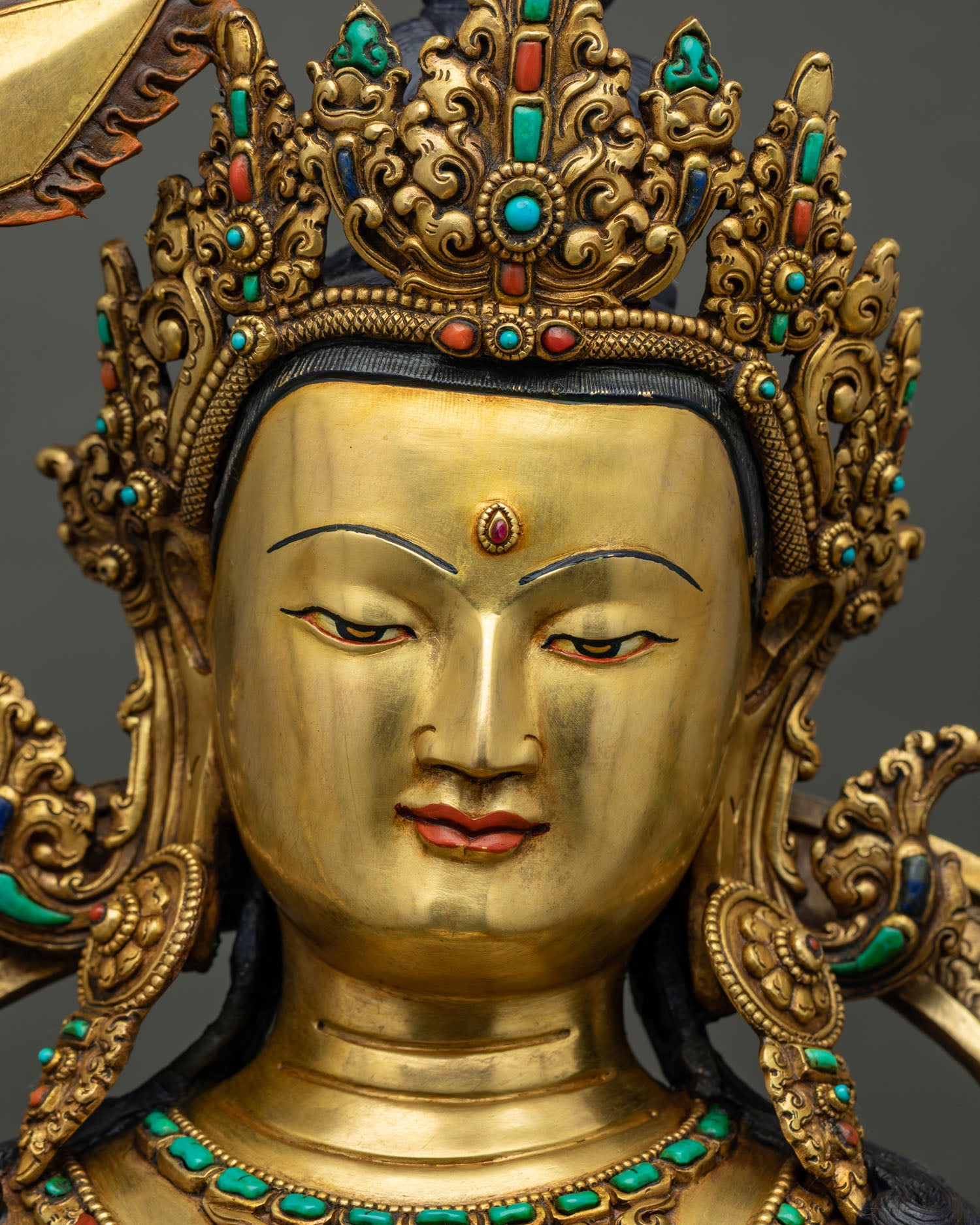 Manjushri statue face close up, gold-painted serene expression with ruby urna and jeweled crown, Nepal
