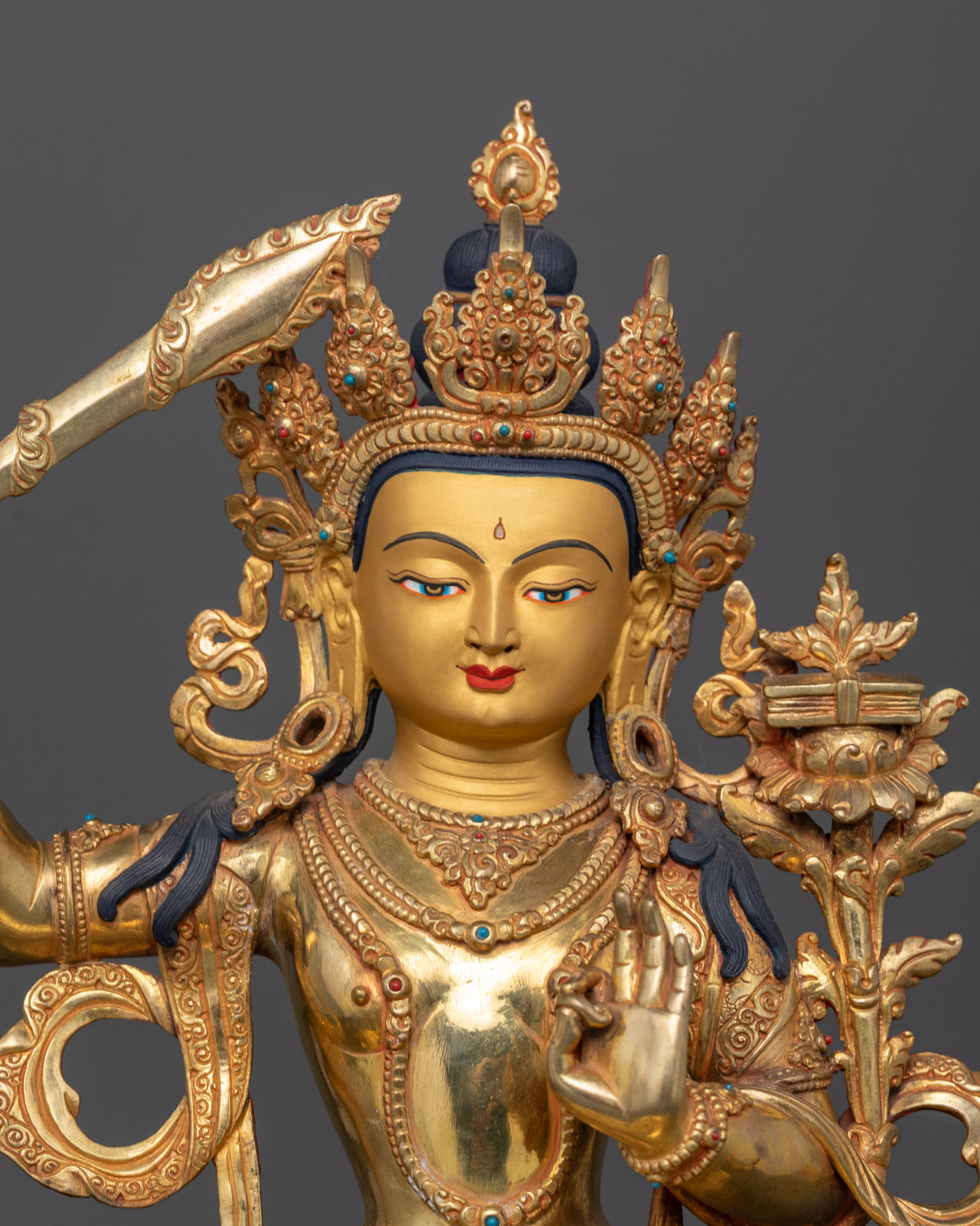 Manjushri wisdom deity seated on lotus pedestal with gold painted face and ornate details