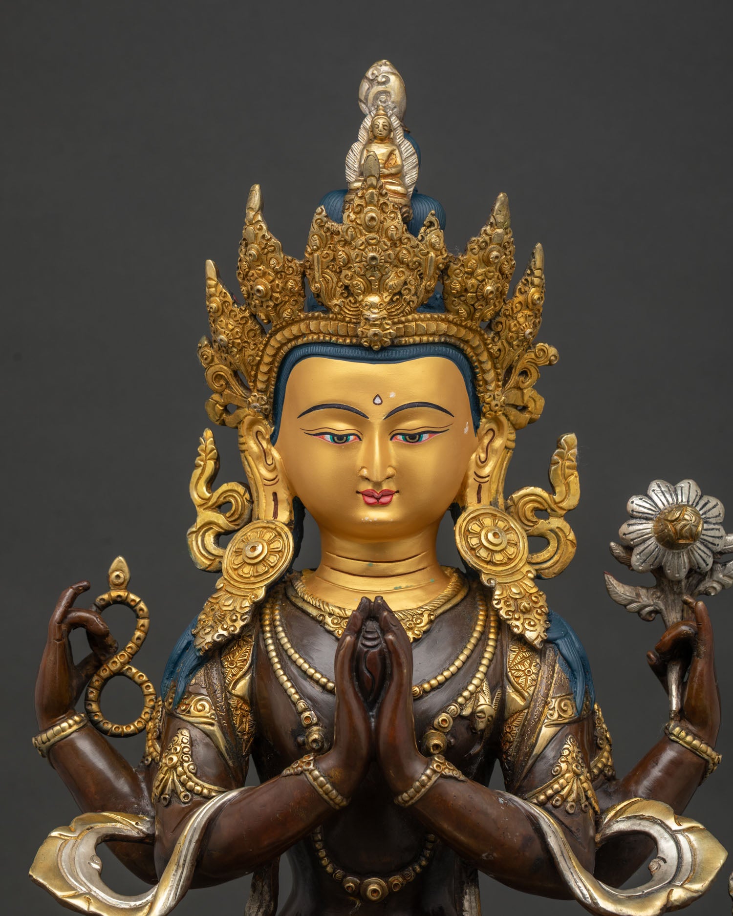 Mid-shot close-up of 4-armed Chenrezig statue holding crystal mala and lotus flower on oxidized copper finish.