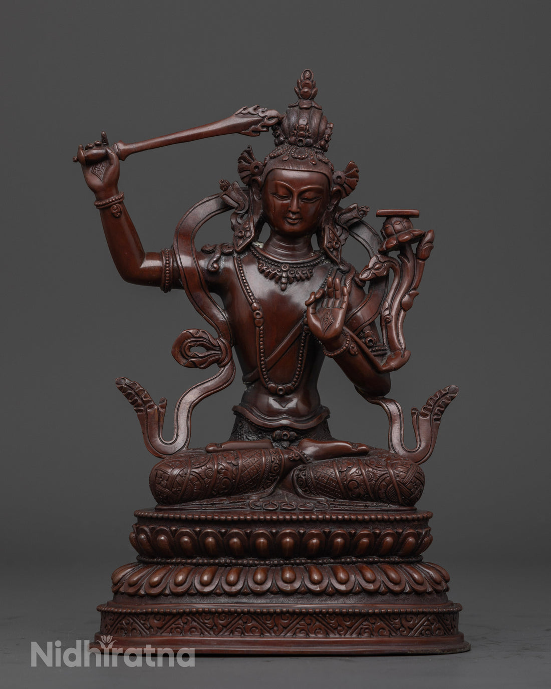 oxidized manjushri statue holding a sword with a book on a flower