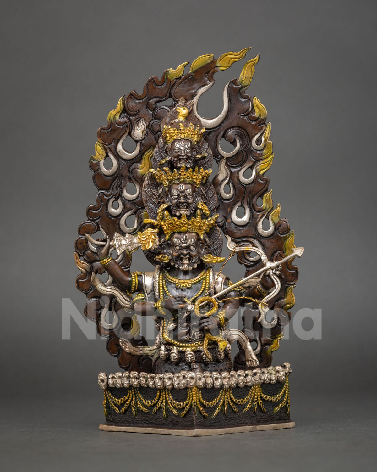 Rahula statue with three stacked heads, bow and arrow, skull base and flame halo in copper