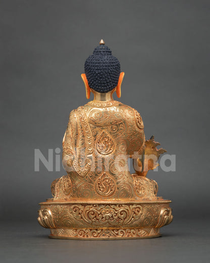 Rear view of gold Medicine Buddha statue with engraved robe and scrolled lotus base