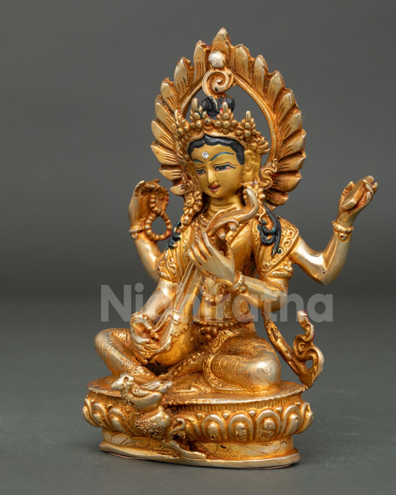 Saraswati Goddess statue seated on lotus base with swan holding veena mala and sacred Vedas.