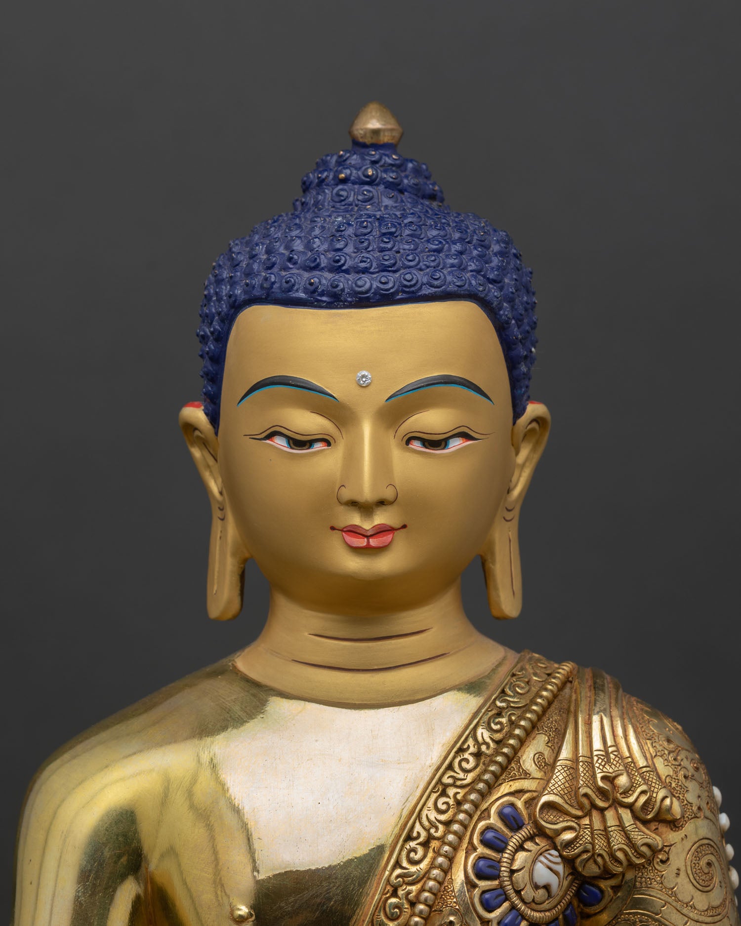 Shakyamuni Buddha face close up with gold painted serene expression and repousse robe with semi precious stones