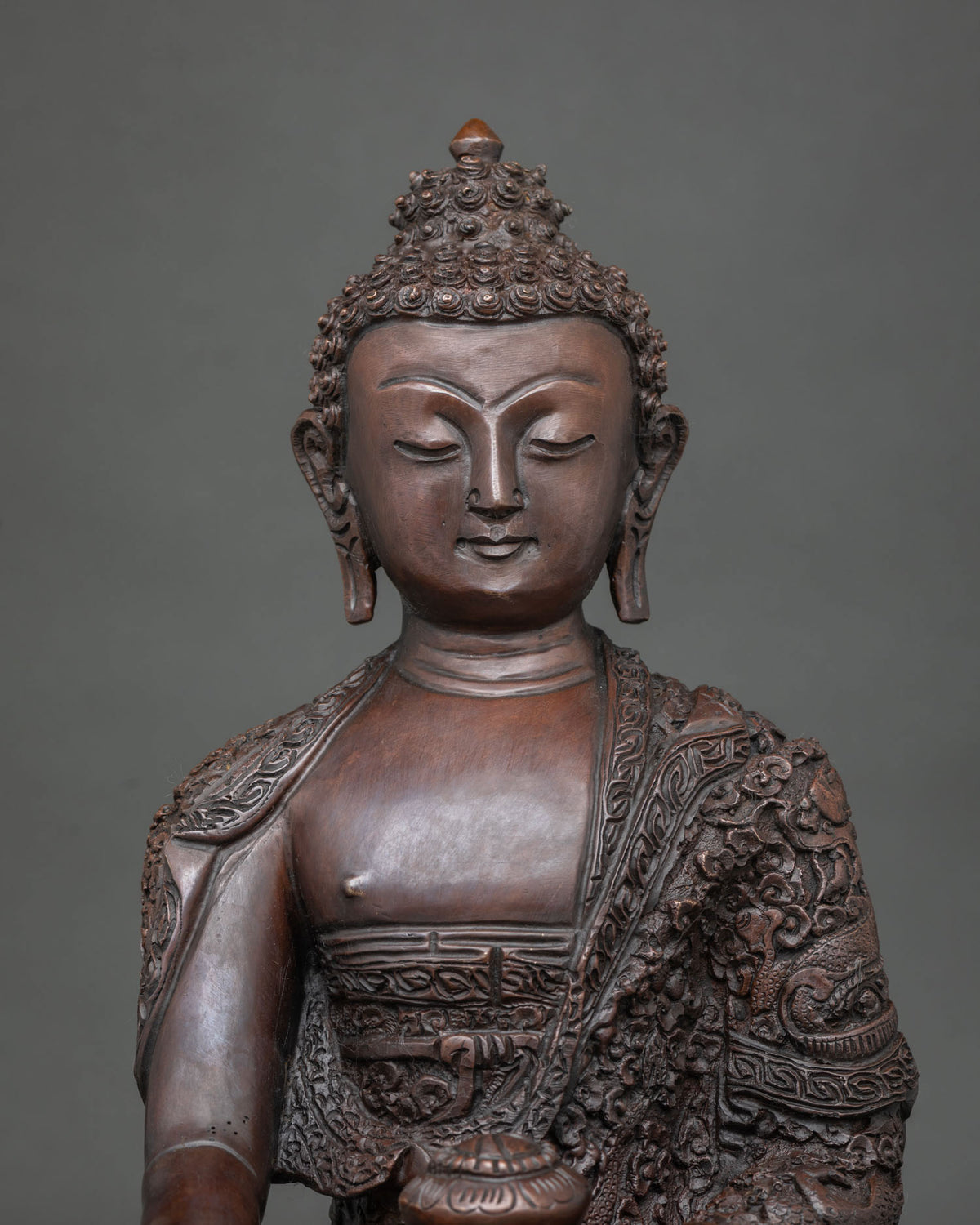 Shakyamuni Buddha statue featuring a finely detailed face and with a traditional chemically oxidized finish.