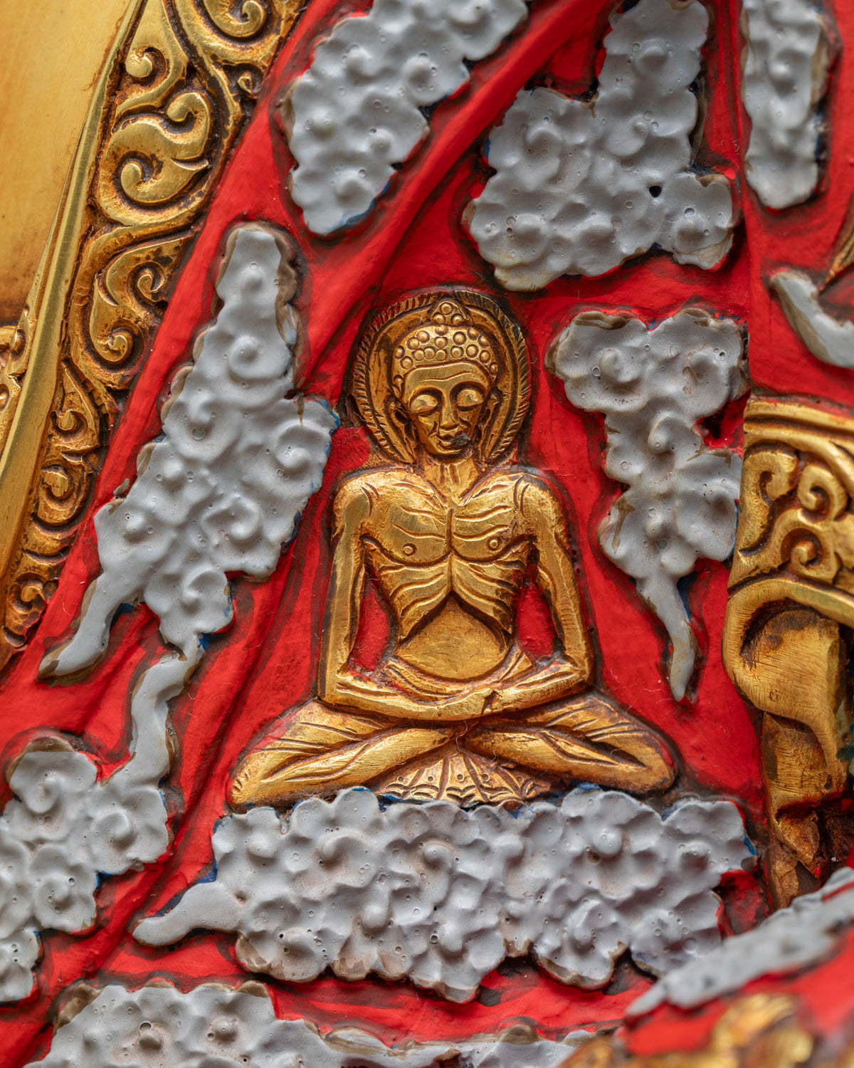 Shakyamuni Buddha statue robe detail showing the ascetic Buddha in gold relief among sculpted clouds