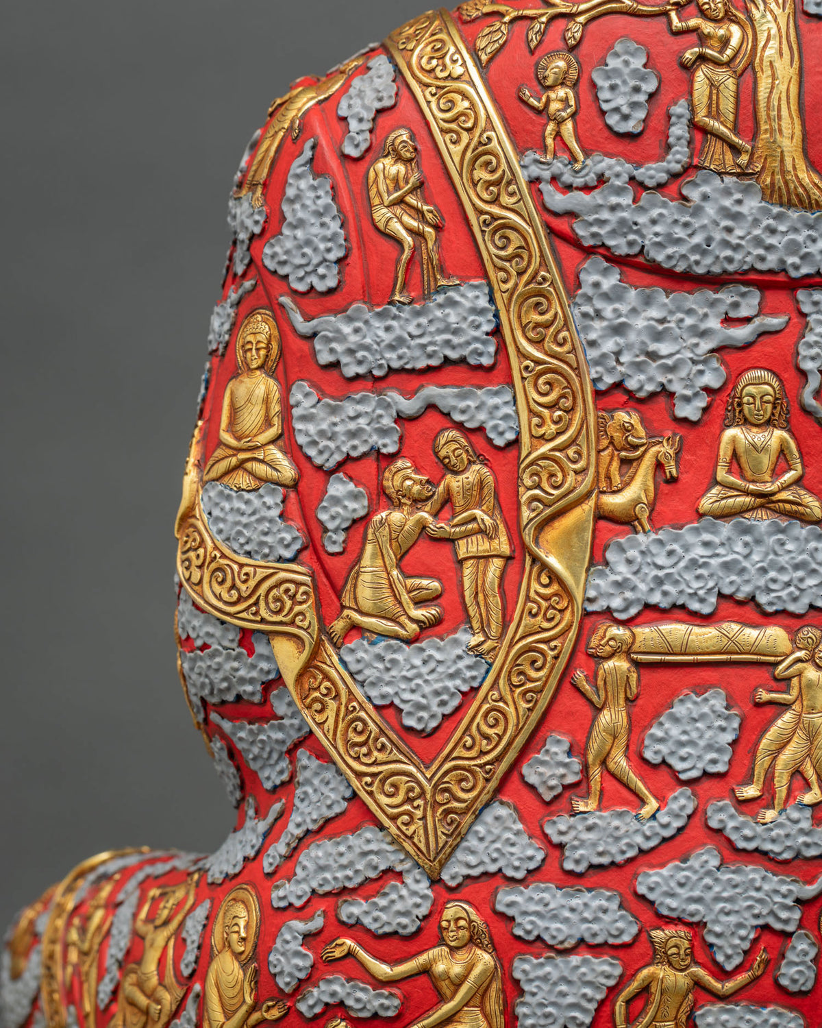 Shoulder detail of Shakyamuni Buddha statue robe with gold relief life scenes and scrollwork border