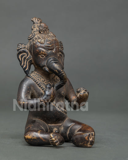 Side angle view of oxidized copper Little Ganesh statue with curling trunk and sweets from Patan, Nepal