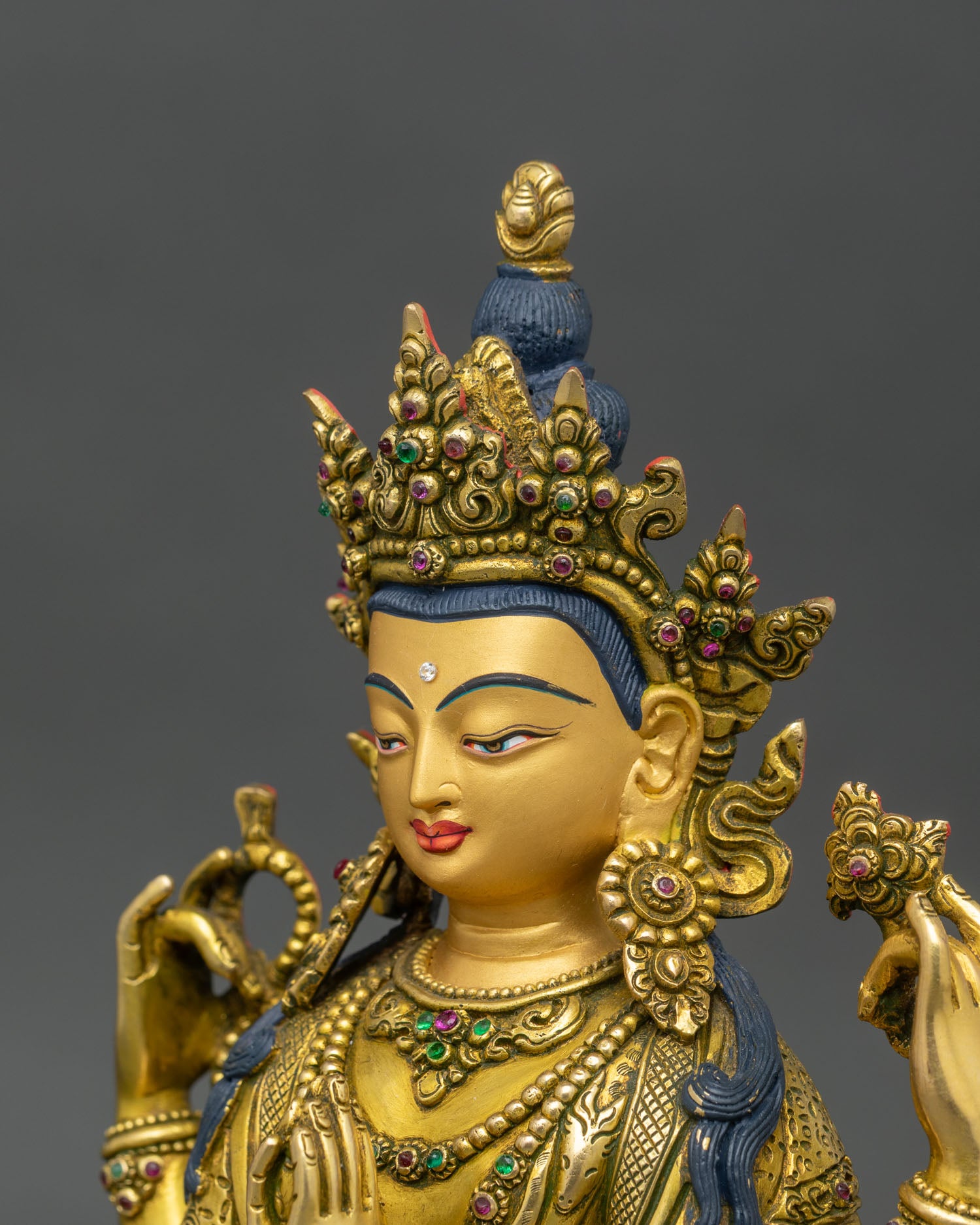 side close-up of chenrezig statue, four arms holding lotus, rosary, and chintamani