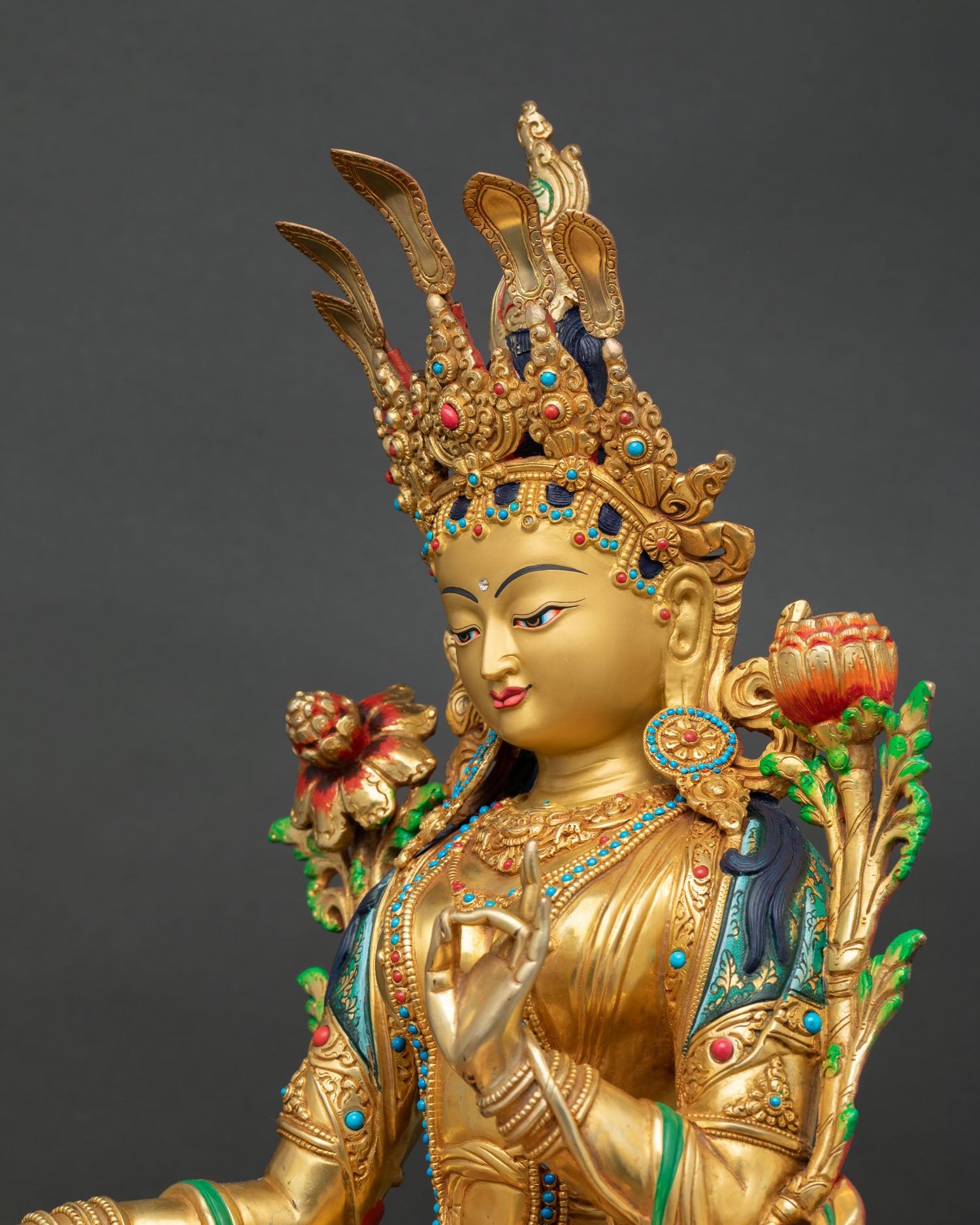 Side close-up of Green Tara statue showing lotus flower stem, painted robes, and gold detailing