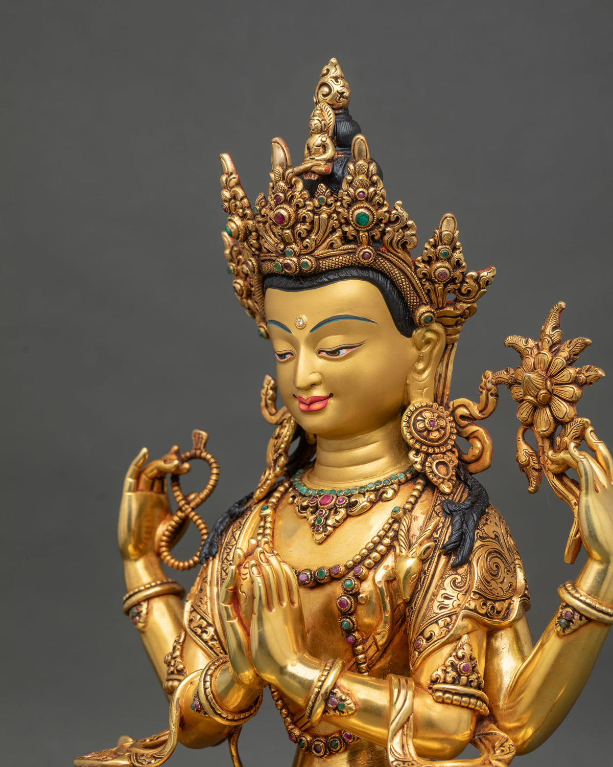 Side close up of hand-carved copper Chenrezig statue with gemstone inlays.