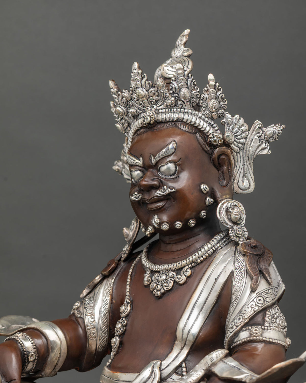 Side close up of hand-carved Dzambhala statue holding citron fruit and jewel-spitting mongoose