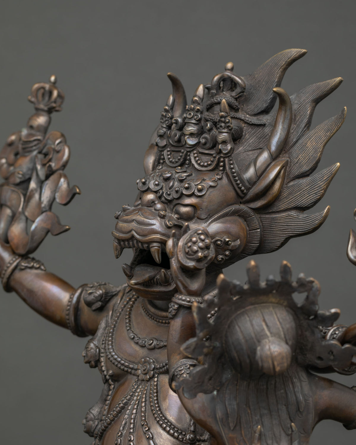 Side close up of Yamantaka statue showing jeweled necklaces, skull garland and flaming hair in copper