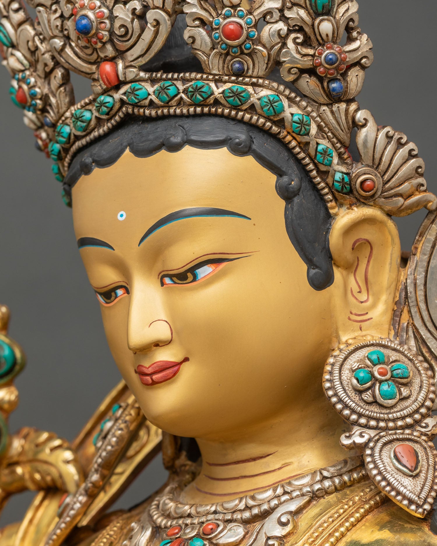 Side face close up of Green Tara statue with gold painted face and stone-set crown