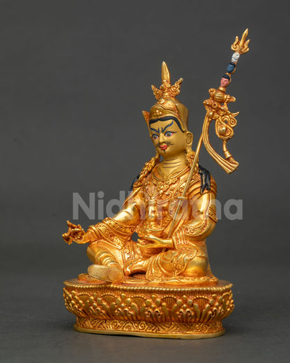Side profile of gold Padmasambhava statue with raised khatvanga staff on lotus pedestal