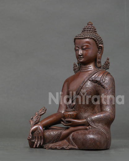 Side profile of oxidized copper Medicine Buddha statue seated with medicine bowl