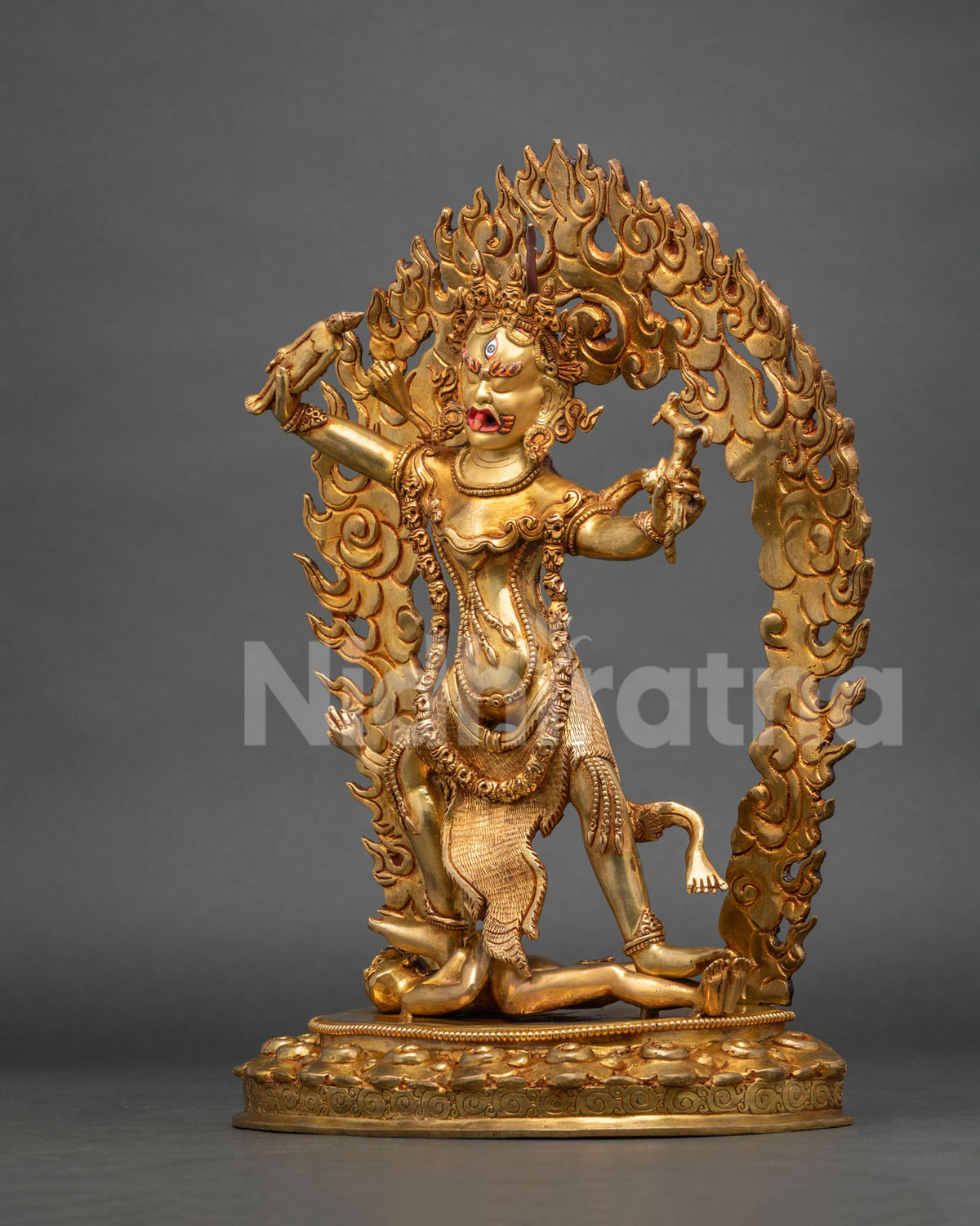 Side profile view of gold gilded Ekajati statue with flame halo and pedestal base