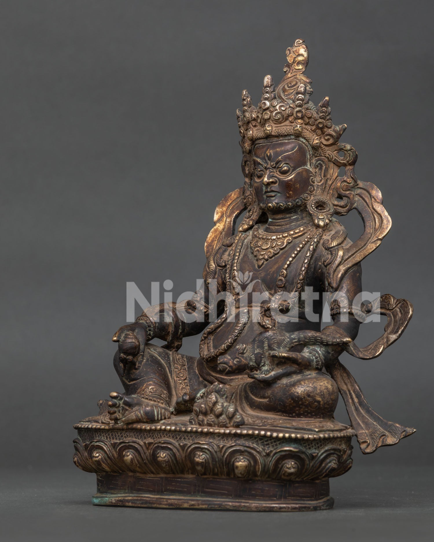 Side view Dzambhala statue showing intricate oxidized copper carving and lotus pedestal.