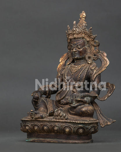 Side view Dzambhala statue showing intricate oxidized copper carving and lotus pedestal.