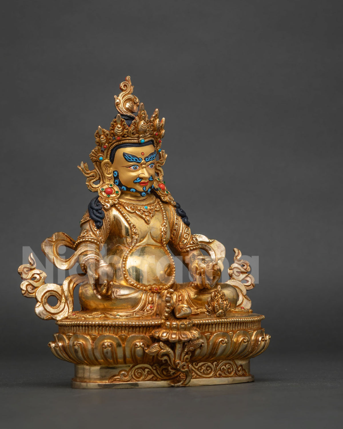 Side view of gold fire gilded dzambhala statue with hand carved floral motifs on royal garments.
