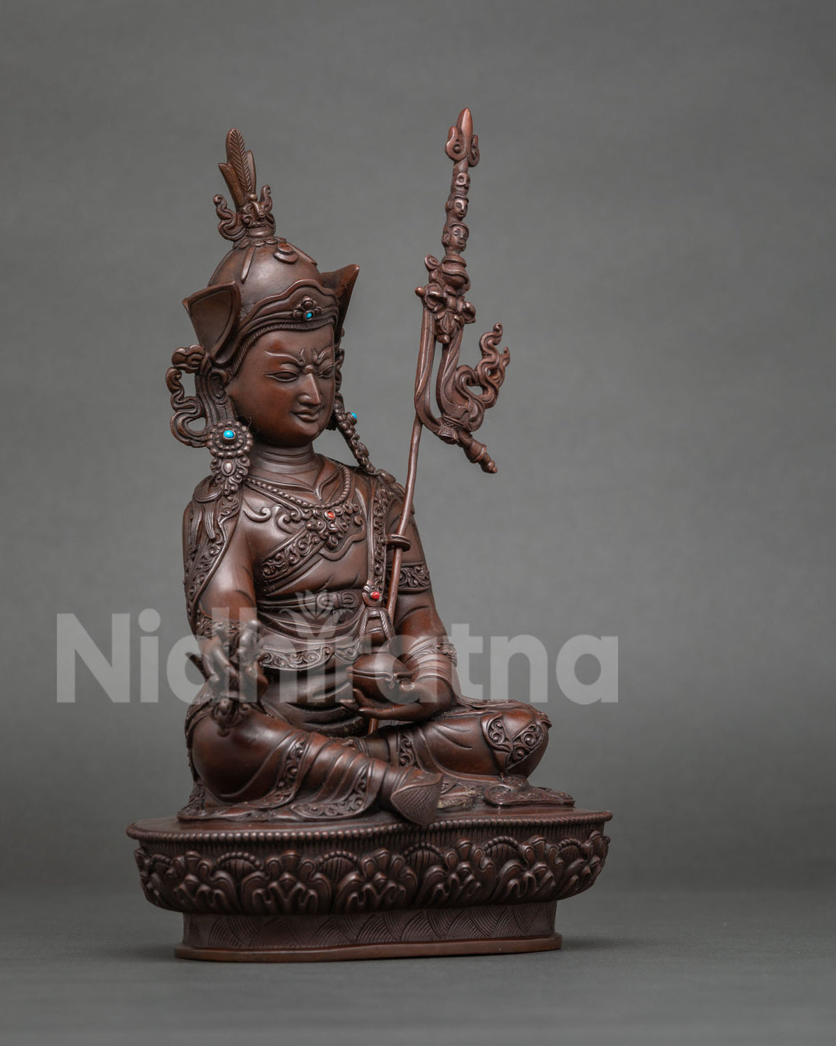 Side view of Guru Rinpoche statue holding a vajra in oxidized copper finish