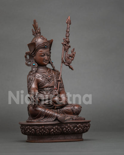 Side view of Guru Rinpoche statue holding a vajra in oxidized copper finish
