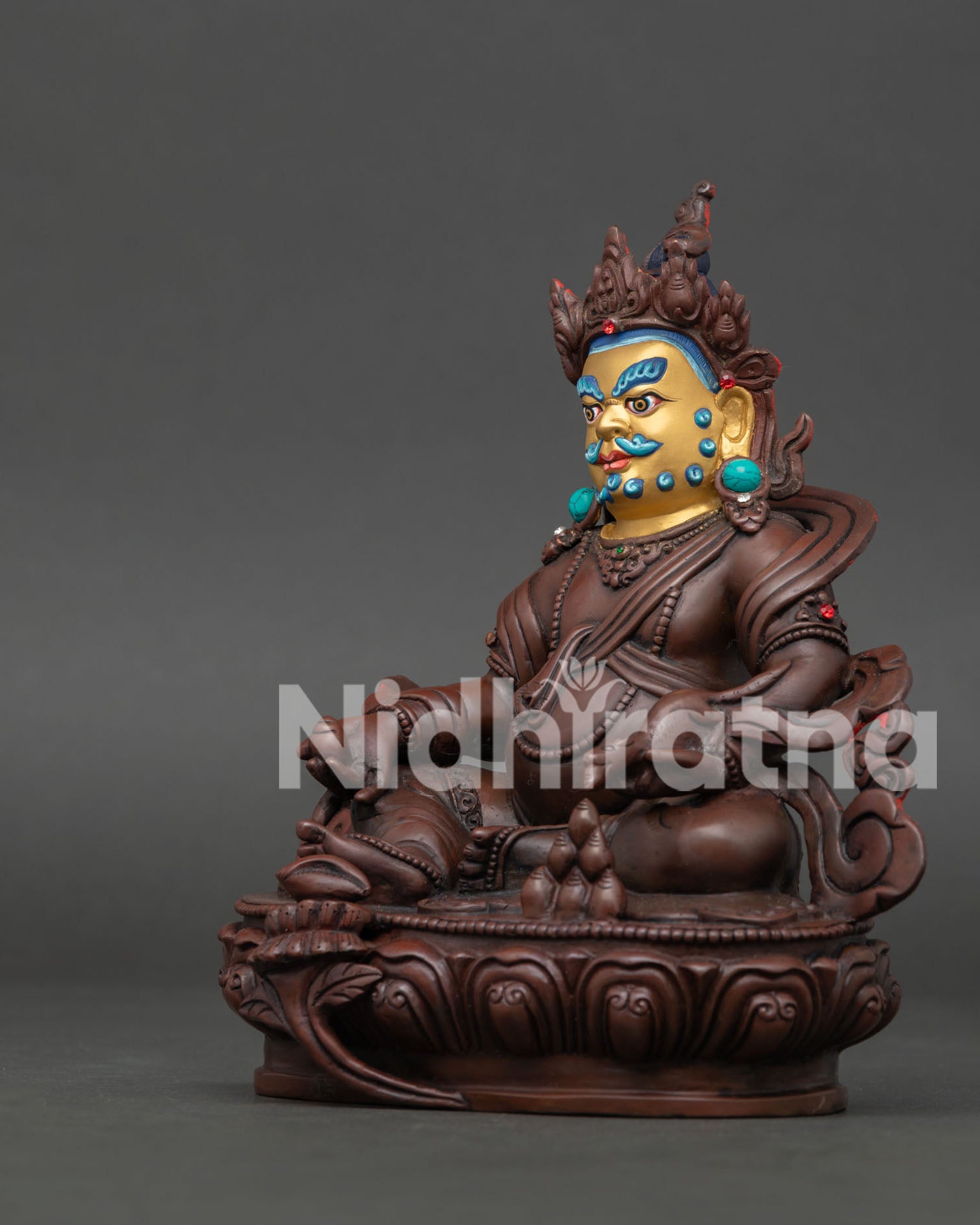 Side view of handmade Dzambhala statue showing lotus throne, mongoose, and flowing robe details.