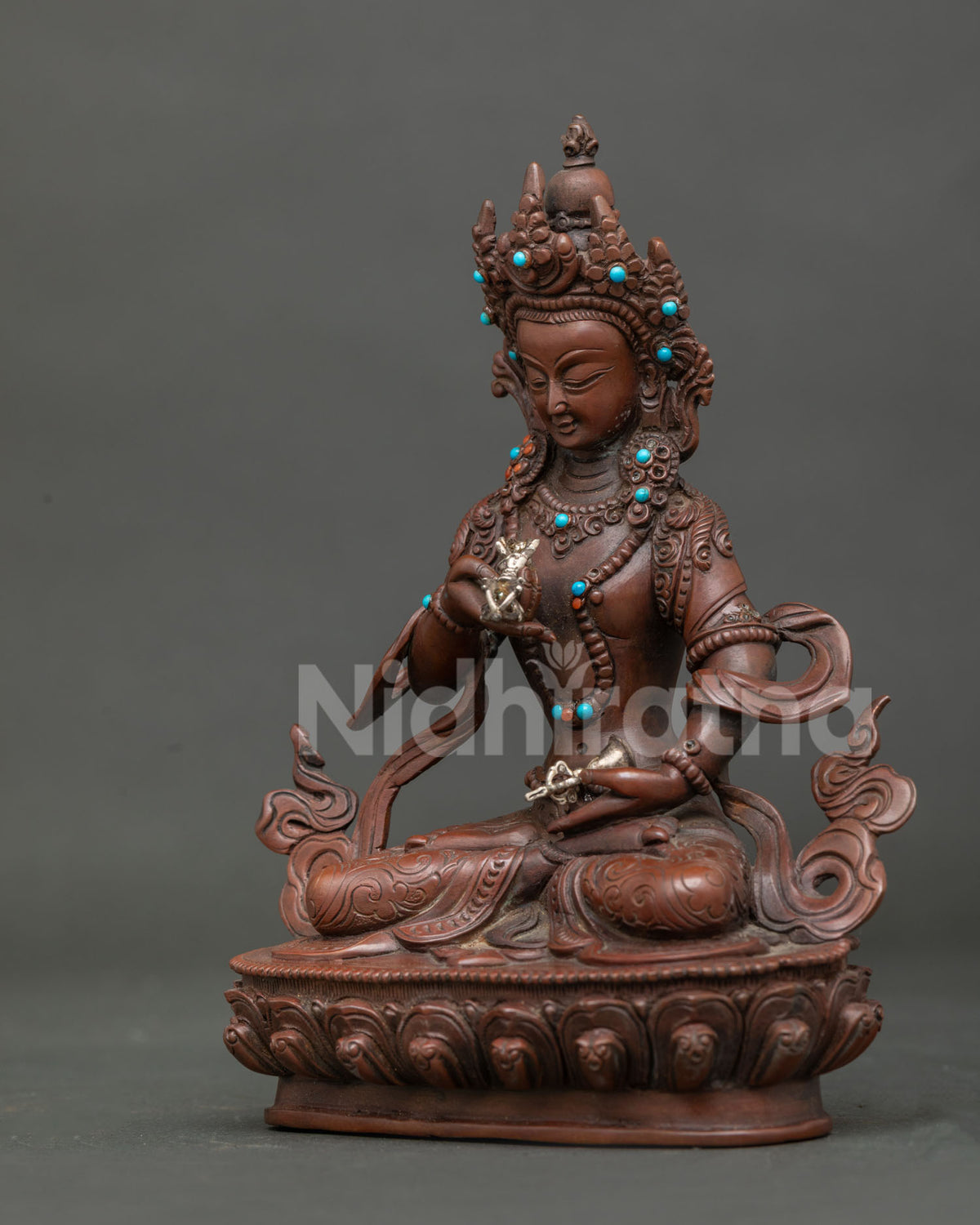 Side view of vajrasattva statue holding five pronged silver vajra and ritual bell.