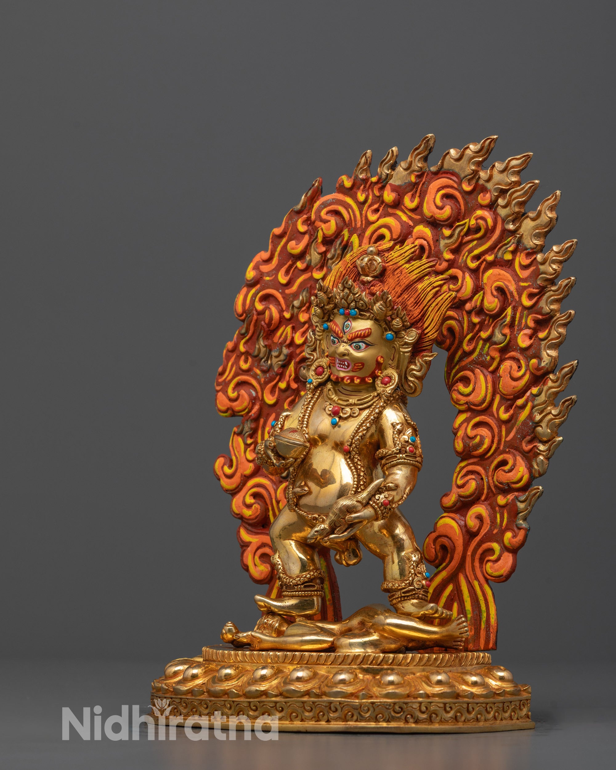 side view of black dzambhala statue with jewel-spitting mongoose and fiery halo symbolism