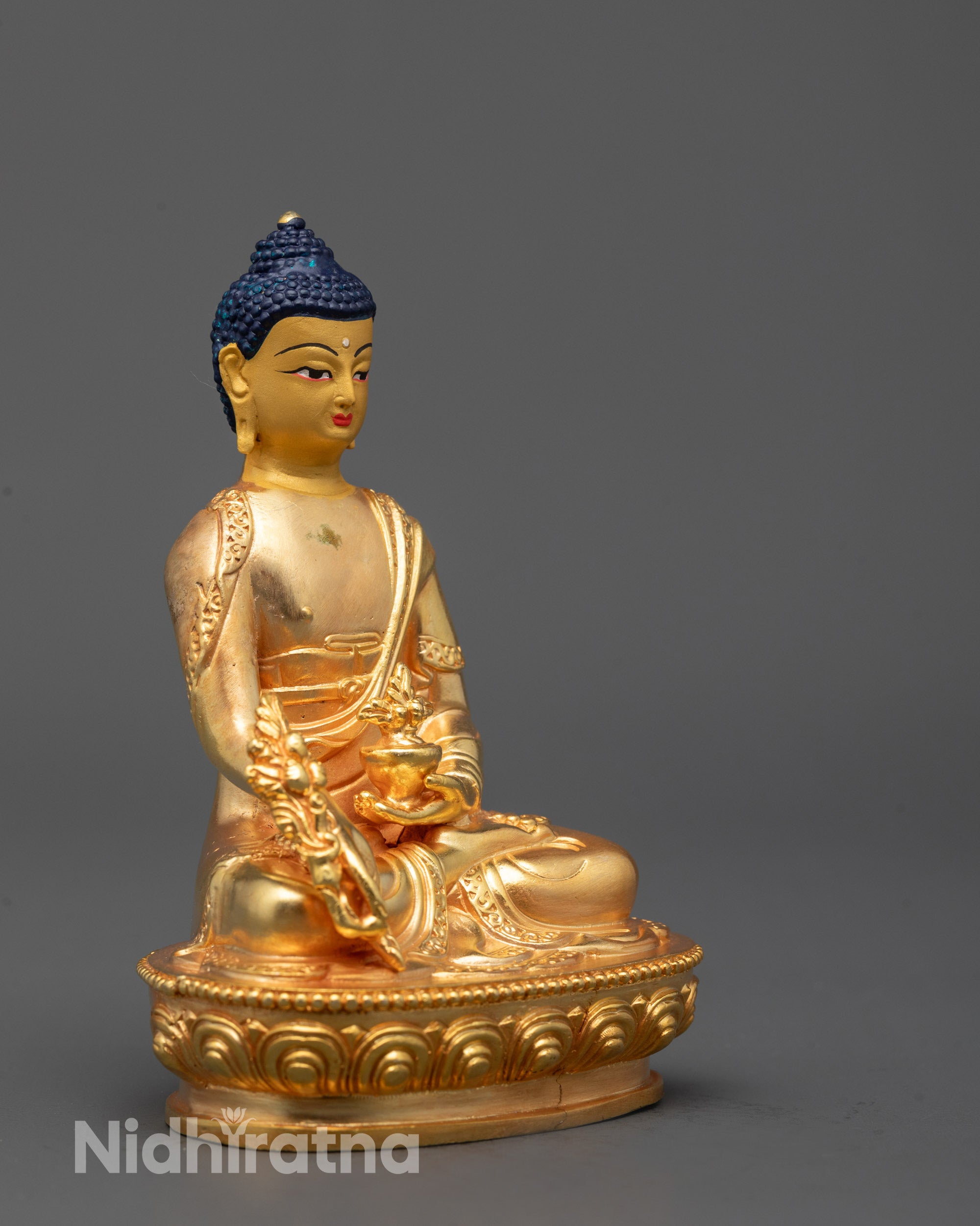 side view of medicine buddha statue holding myrobalan plant in monk robe on lotus seat
