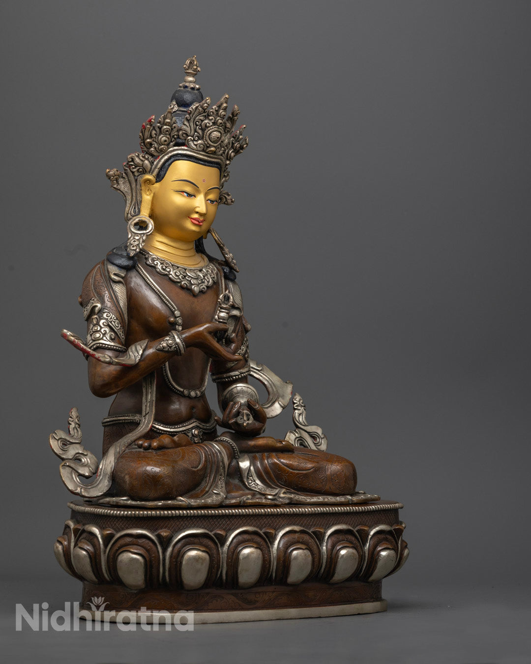side view of vajrasattva statue holding vajra and bell with calm expression and silver robe