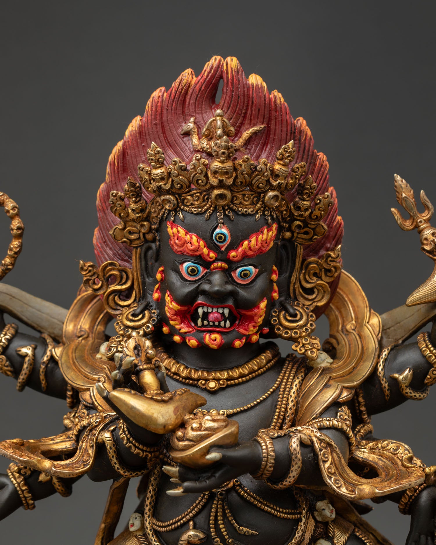 Six-armed Mahakala statue front close-up, showcasing the fierce facial expression, third eye, and intricate ornamental detailing.