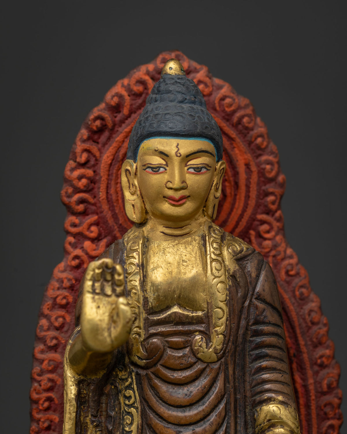 Standing Buddha statue close up gold painted face red gold halo and lotus throne.