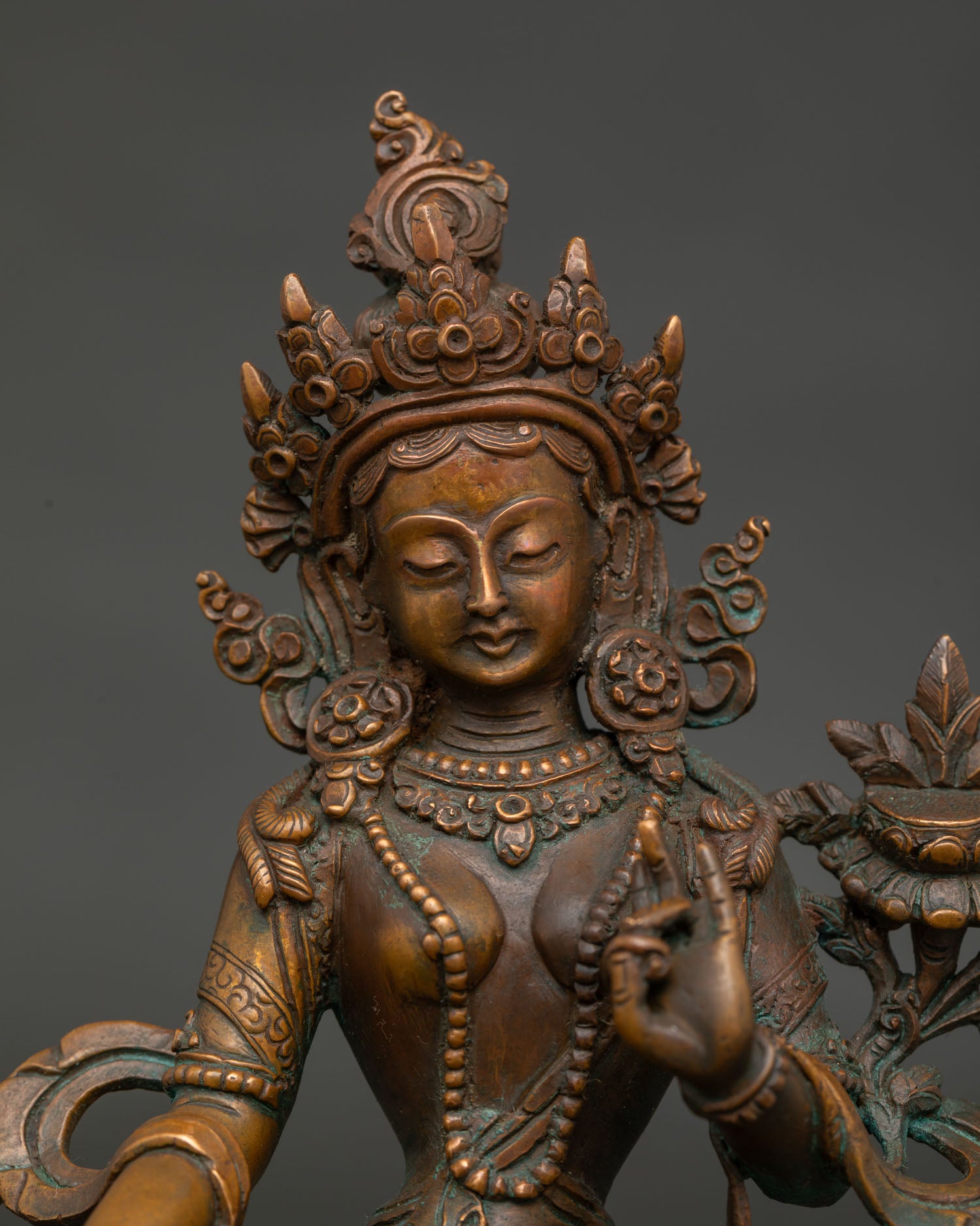 Green Tara statue face with serene expression five jewel crown and lotus.